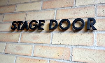 a sign reading "Stage Door" on a brick wall