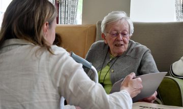 A young woman in a white shirt showing a booklet to an older woman