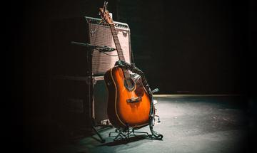 A dark stage with a spotlight on an amp and an acoustic guitar