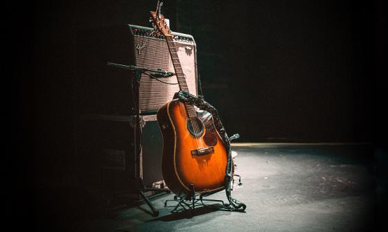A dark stage with a spotlight on an amp and an acoustic guitar