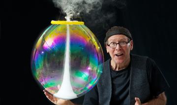 The Amazing Bubble Man stood against a black background holding a colourful bubble tornado
