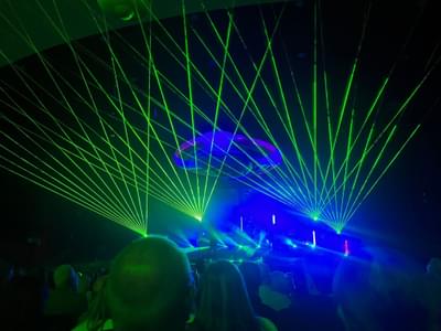 Green lasers and blue lights coming from the stage where the band are performing to a very excited audience