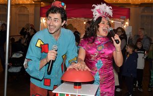 Aladdin and Jasmine both look excited as they both hold one hand over the large red button and hold microphones in their spare hand