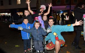 Jasmine stands behind a large group of children, three boys and one girl, Aladdin crouches down to the side and all pose with their arms held out