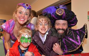 Spirit of the Ring and Abanazer smile for the photo with a young boy and girl, both children have their faces painted, one like a dragon, the other like a reindeer