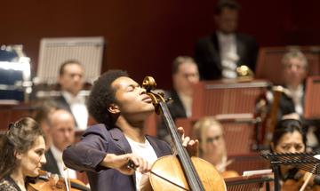 Sheku Kanneh-Mason playing the cello with the Philharmonia Orchestra, on stage at the Anvil at the 25th Anniversary Gala concert