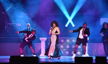 Belinda Davids as Whitney Houston performing on stage, with two male dancers either side of her