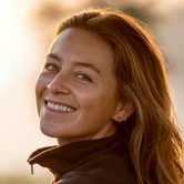 A white woman with dark blonde hair in a black fleece smiling over her shoulder