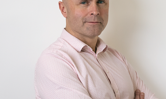 Garry Hurry wearing a pink shirt with his arms folded looking at the camera