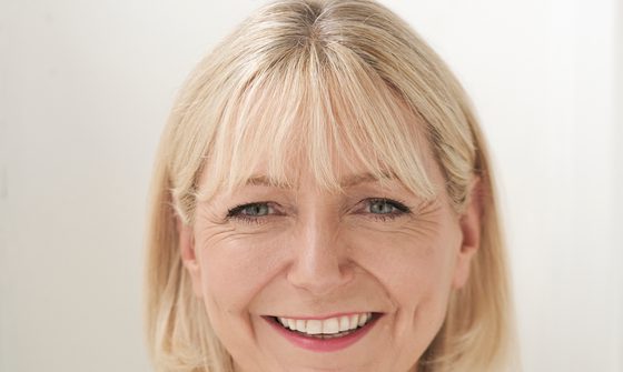 Sarah Jane Buckley, an older white woman with light blonde hair smiling at the camera in a green top with white flowers
