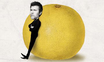Black and white image of Rhod Gilbert's head on a smaller body wearing all black with his arms crossed, leaning against a colourful grapefruit