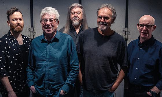 Five members of 10cc stood in a line, smiling at the camera
