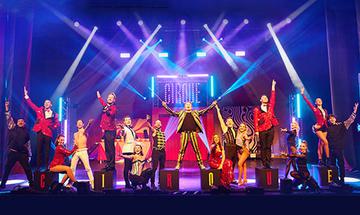 Multiple circus performers on stage in a line facing the audience with strobe lights around them