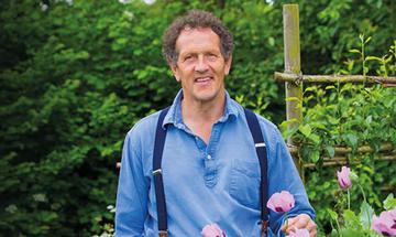 Monty Don in a green garden with pink flowers at the forefront.