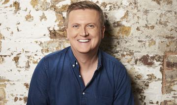 Aled Jones stood in front of a wall laughing.