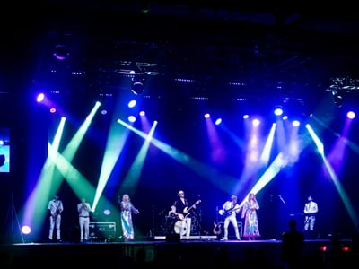 A vibrant live concert scene with a band on stage, colourful spotlights in blue, purple, and green hues