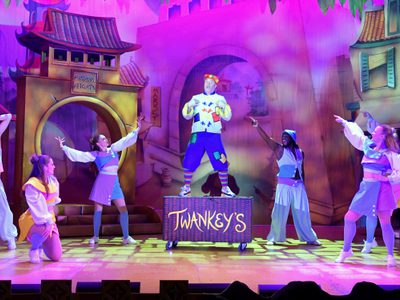 Wishee Washee is stood on a laundry basket with the ensemble around him