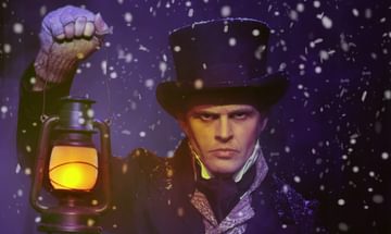 An actor dressed as Scrooge on a snowy night holding a lantern in his right hand with a stern expression on his face
