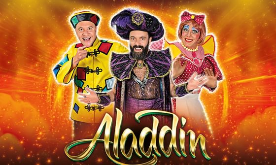Chris Pizzey dressed as Wishee Washee, James Mackenzie as Abanazar, and Nic Gibney as Widow Twankey against a orange sparkly background with the words "Aladdin" in gold