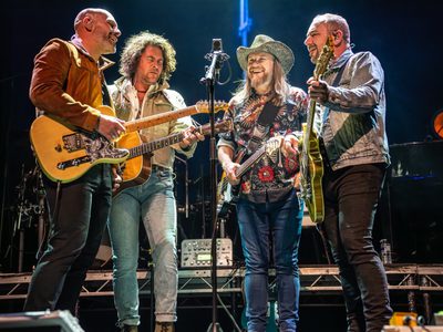 Four male guitarists stand around one microphone as they all sing