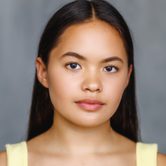 An Asian woman with long straight black hair in a yellow top looking at the camera with a neutral expression