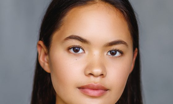 An Asian woman with long straight black hair in a yellow top looking at the camera with a neutral expression