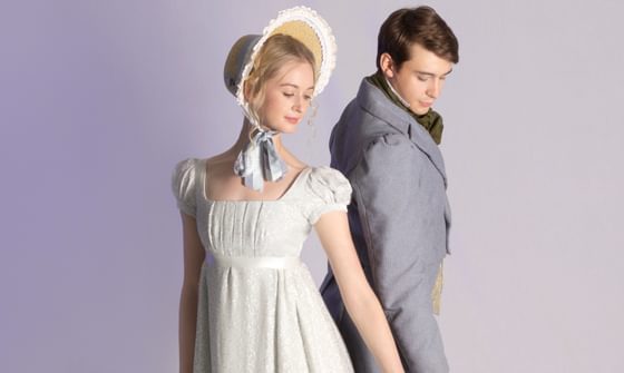 Two ballet dancers – one female wearing a cream dress and matching bonnet, and a male in a grey suit. They are looking at the floor with one hand touching
