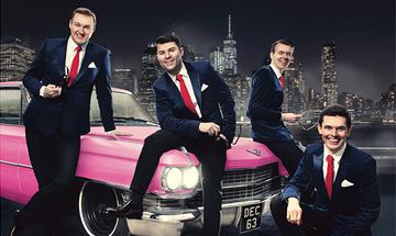 Four men in black suits with white shirts and red ties sat on a pink car with a black and white city skyline behind them