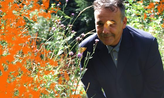 Rob Newman wearing a suit outdoors, smiling near some wildflowers and orange foliage