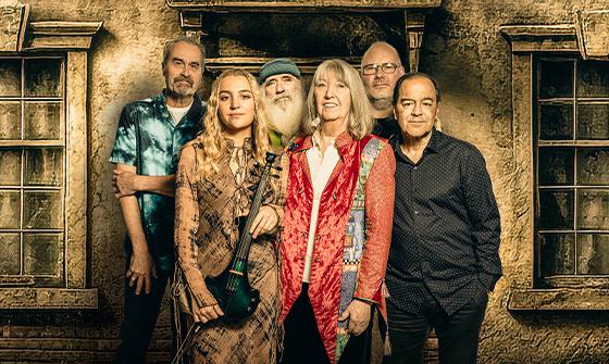 Six members of Steeleye Span posing against a textured wall with vintage-style windows