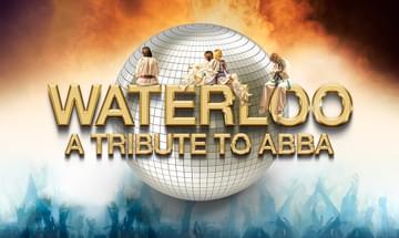 A disco ball with gold text over it that reads 'Waterloo A Tribute To ABBA' with 4 members of ABBA sat on the letters. The background is an ombre from a dark, to orange, to white, to blue. It looks like the disco ball is on fire with where the orange is, and in the blue is the silhouette of a crowd with their arms up