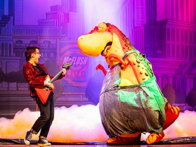 Danny wears a red blazer jacker and plays his red guitar while Dino dances