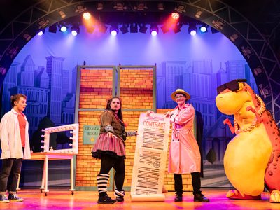 Two women hold out a huge contract which hits the floor, either side of them Danny and Dino look on in shock