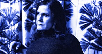 A photo of Alison Moyet in a turtleneck jumper with floral curtains behind. the whole image has a blue hue