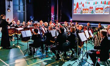 A band performing on the floor of a gym hall in Christmas hats with a festive PowerPoint behind them