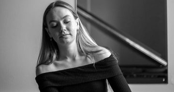 A black and white photo of a young white woman in a black top playing piano