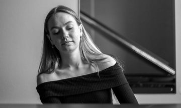 A black and white photo of a young white woman in a black top playing piano