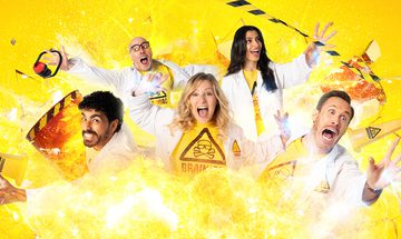 Five scientists in lab coats, two women and three men all jump with excitement behind a large explosion