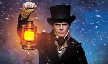 A grumpy white man in a top hat, shirt, cravat, waist cost, duffle coat, and fingerless gloves holding a lantern in the middle of snow