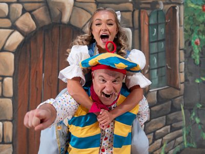 Chris Pizzey giving Ellie Dadd a piggy back ride. Both are smiling/screaming with their mouths wide open and Chris is pointing directly at the camera