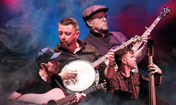 Four white men all in dark shirt, t-shirts, and jackets playing various string instruments including two banjos, a guitar, and a double bass