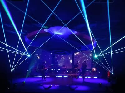 The band on stage in low light with blue lights and lasers on stage