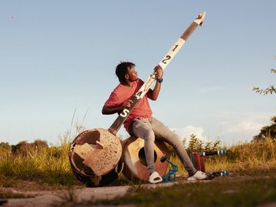 Gasper Nali, a black man with mid-length braided hair playing the babtoni in a field