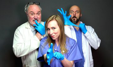 Three people, two men and a woman, all stood in doctors uniforms playing with blue rubber gloves