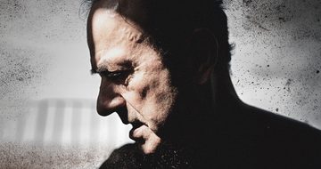 A dark image of Hugh Cornwell with only his face lit on a distressed grey background