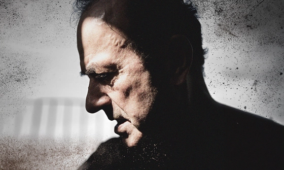 A dark image of Hugh Cornwell with only his face lit on a distressed grey background