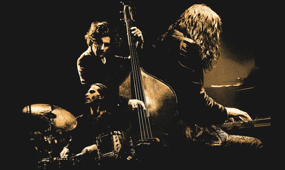 A sepia image of a drummer, a pianist and a cellists all performing