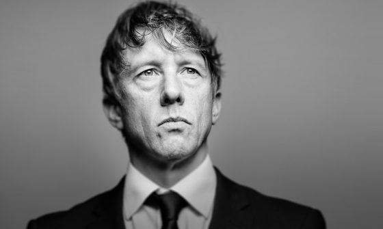 Jonathan Pie looks stern as he stands dressed in a suit.