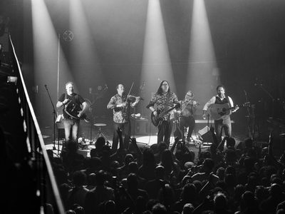 All five members of the band perform on stage in front of a packed crowd
