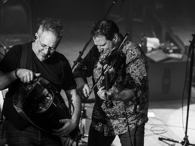 A man plays a hurdy-gurdy while his bandmate stands next to him playing the fiddle